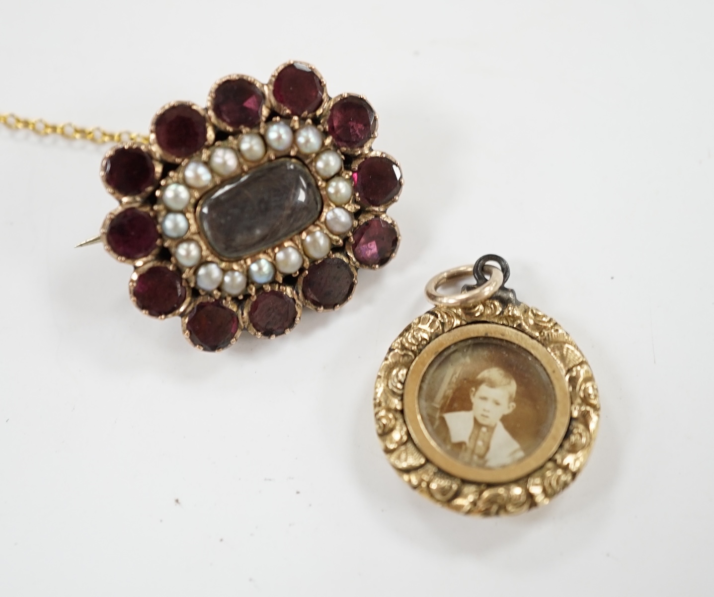 An early Victorian yellow metal, garnet and split pearl set mourning brooch, with engraved monogram, 23mm and a George IV mourning locket, inscribed 'Martha Lloyd, ob. 8th May, 1824 at 53'. Condition - fair